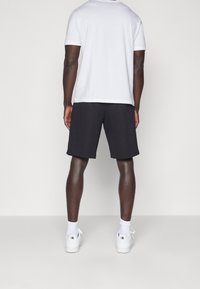 Manlig bakvy iförd en figursydd vit bomull T-shirt och svarta shorts. Kompletterad med vita sneakers med mönstrade detaljer.