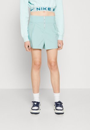 Lyseblå shorts med høyt liv og glidelås foran, med to skrå lommer og en glatt tekstur. Stylet med en matchende topp og sneakers.