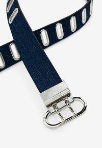 Dicker blauer Denim-Gürtel mit silberner Metallschnalle. Verfügt über ovale Aussparungen entlang des Gürtels für eine verstellbare Passform und Design-Details.
