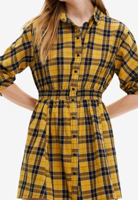 Donna che indossa un abito a quadri giallo e blu navy con vita elasticizzata e maniche arrotolate.