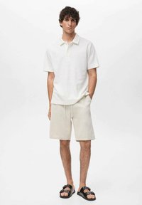 Hvid tekstureret polo skjorte, cremefarvede shorts og sorte sandaler. Outfittet har en klassisk krave og en afslappet pasform med sidelommer.