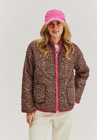 Kurtka puchowa w panterkę z różowym zamkiem błyskawicznym i wykończeniami, posiadająca dwie przednie kieszenie. W połączeniu z różową czapką, noszoną na białej bluzce.