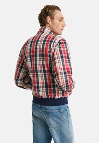 Bomber jacket a quadri rossi, blu navy e beige con colletto e polsini a coste, abbinato a jeans in denim azzurro chiaro. La giacca presenta una vestibilità comoda.