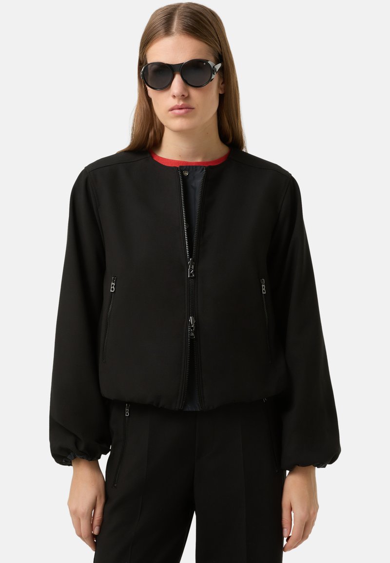 Czarna kurtka bomberka z zaokrąglonym dekoltem, z przodu zapięcie na zamek błyskawiczny oraz dwie boczne kieszenie na zamek. Posiada bufiaste rękawy i czerwoną podszewkę wewnętrzną.