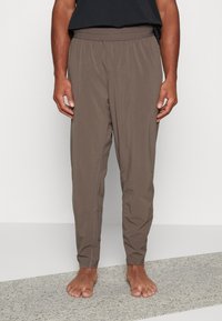 Brune letvægtsbukser med elastisk talje, tapered ben og to sidelommer. Glat tekstur med synlige sy detaljer.