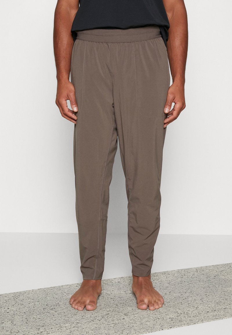 Brune letvægtsbukser med elastisk talje, tapered ben og to sidelommer. Glat tekstur med synlige sy detaljer.