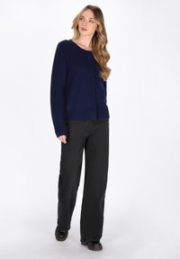Navyblauer Cardigan mit rundem Halsausschnitt, Knopfleiste und gerippten Bündchen, kombiniert mit schwarzen weit geschnittenen Hosen und schwarzen Schuhen.