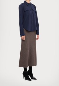 Chemise bleu marine à boutons, avec deux poches poitrine, associée à une jupe midi côtelée marron et des escarpins noirs à bout pointu, avec des brides à la cheville.