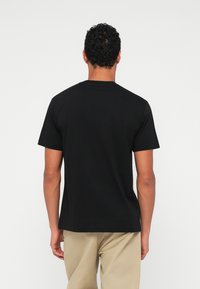 Juodas medvilninis marškinėlis su trumpomis rankovėmis ir apvaliu iškirpimu, turi lygų paviršių ir derinamas su bežinėmis kelnėmis.