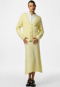 Mjukt, ljusgult stickat kortkart med V-hals och sex knappar som matchas med en kjol. Slät textur med långa ärmar och avslappnad passform.