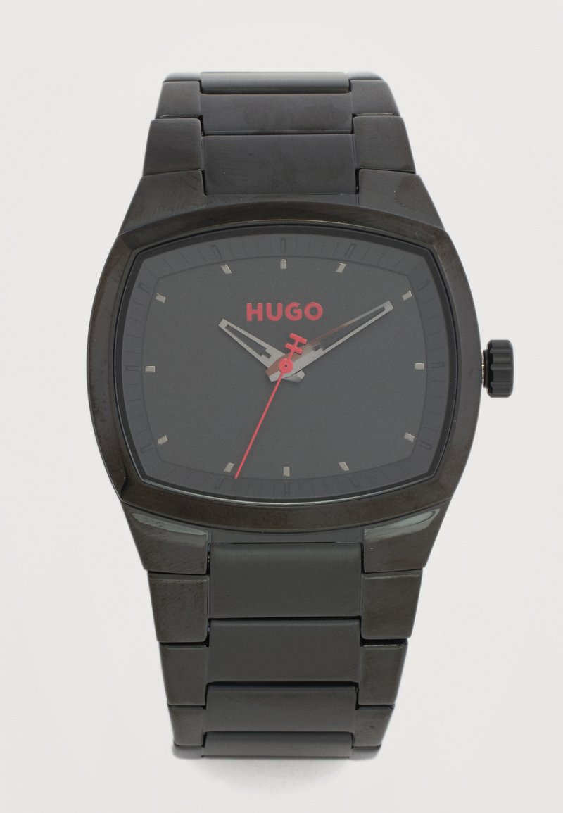 Μαύρο μεταλλικό ρολόι χειρός με ορθογώνιο καντράν, ασημένιους δείκτες ώρας, κόκκινο δευτερόλεπτο και κόκκινο λογότυπο "HUGO" στο καντράν.