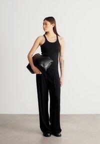 Μαύρο αμάνικο τοπ και πλισέ παντελόνια με φαρδιά πόδια, συνδυασμένα με μεγάλη μαύρη δερμάτινη τσάντα. Λεία υφή και μινιμαλιστικός σχεδιασμός.