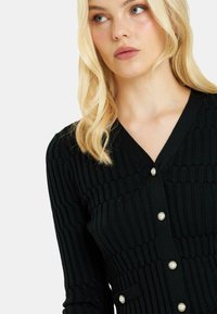 Schwarze, gerippte Strickjacke mit V-Ausschnitt, Perlenknöpfen und strukturiertem Schnitt. Textil mit vertikalen Mustern.