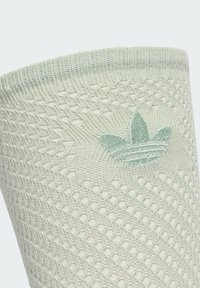 Svetlozelená pletená tkanina s vzorom sieťky, na ktorej je vyšité logo Adidas trefoil v zodpovedajúcej zelenej farbe na bielom pozadí.