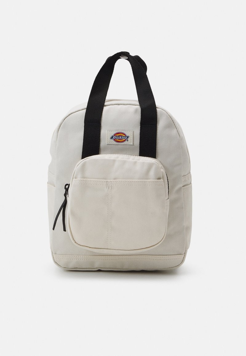 Sac à dos en toile beige avec poignées noires, poche zippée avant et petite étiquette de logo colorée centrée au-dessus de la poche.