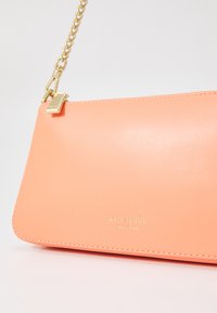 Pink leather shoulder bag with a gold chain strap. Features stitched edges and a gold logo embossed on the front. Simple, rectangular shape.