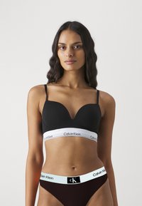 Svart polstret bh med justerbare stropper og en hvit Calvin Klein logobånd. Kombinert med mørkerøde undertøy og CK logobånd.