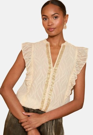 Beige blouse with ruffled sleeves and a V-neck, featuring a textured pattern and a central gold trim with buttons down the front.