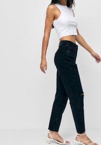 Černé džínové kalhoty s vysokým pasem a roztrhanými detaily, spárované s bílým zkráceným topem a bílými sandály na podpatku. Hladká tkanina, přiléhavý střih.