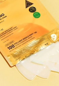 Hydrogelmaskförpackning i metalliskt guld med svarta och gröna accenter. Masken är genomskinlig och glänsande, placerad delvis utanför förpackningen.