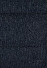 Czarna tkanina w jodełkę o teksturowanej powierzchni, z naprzemiennymi diagonalnymi wzorami i subtelnymi odcieniami niebieskiego i czarnego.