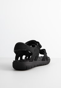 Sandalias ajustables negras con una suela texturizada, que cuentan con múltiples correas para soporte y un diseño abierto para transpirabilidad.
