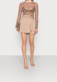 Långärmad, genomskinlig topp med leopardsmönster i brunt och lila; parat med en beige, omslagstyp mini-kjol och gyllene klacksandaler.