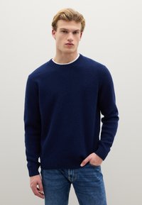 Marineblauer Strickpullover mit rundem Ausschnitt, gerippten Bündchen und strukturiertem Muster. Kombiniert mit blauen Jeans.