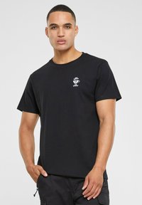 Sort bomuld t-shirt med et lille hvidt tryk på venstre bryst. Korte ærmer, rund hals, standard pasform.