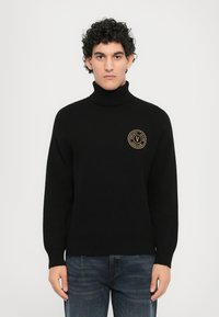 Črna pulover s turtleneck ovratnikom in rebrastimi manšetami ter robom. Na prsih ima zlat krogast logotip. Narejen iz mehkega, strukturiranega blaga.