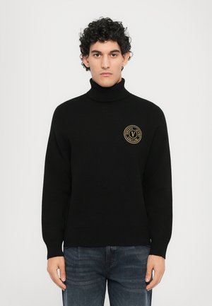 Suéter negro de cuello alto con puños y dobladillo acanalados. Presenta un logo circular dorado en el pecho. Hecho de una tela suave y con textura.