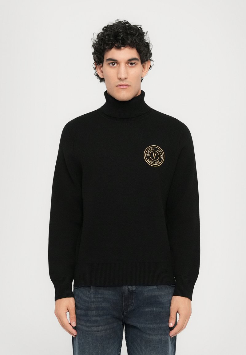Črna pulover s turtleneck ovratnikom in rebrastimi manšetami ter robom. Na prsih ima zlat krogast logotip. Narejen iz mehkega, strukturiranega blaga.