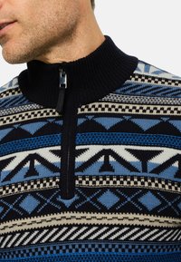 Strickpullover mit hohem Kragen, mit blauen, schwarzen und cremefarbenen geometrischen Mustern sowie einem Reißverschluss am Hals.