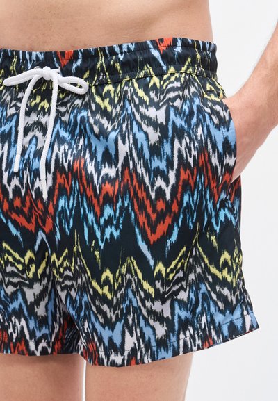 Μαύρο μαγιό σορτς με ζωηρό ζικ-ζακ μοτίβο σε κόκκινο, μπλε, κίτρινο και λευκό. Διαθέτει λευκό κορδόνι και πλαϊνές τσέπες.