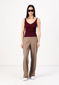 Bordeaux geribbeld tanktop, tan wijde broek en witte sneakers. Model draagt oversized bruine zonnebril. Eenvoudig, modern silhouet.