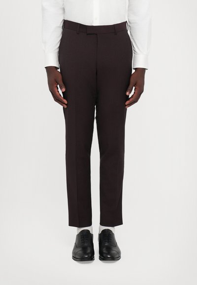Pantaloni sartoriali marrone scuro con una texture liscia e una vestibilità slim, dotati di tasche laterali e fronte piatto, abbinati a scarpe in pelle nere.