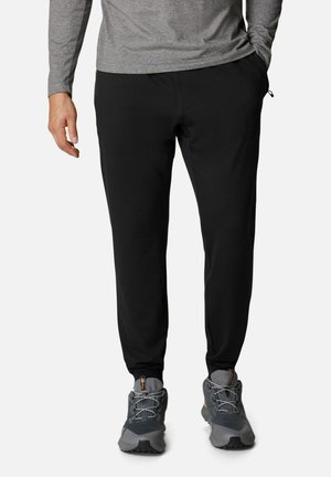 Pantaloni sportivi neri a sigaretta realizzati in tessuto morbido ed elastico, dotati di una cintura elastica e tasche laterali funzionali, indossati con scarpe da ginnastica grigie.