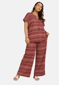 Top a righe rosso e arancione con scollatura a V e maniche corte, abbinato a pantaloni a gamba larga coordinati. Indossato con sandali bianchi.