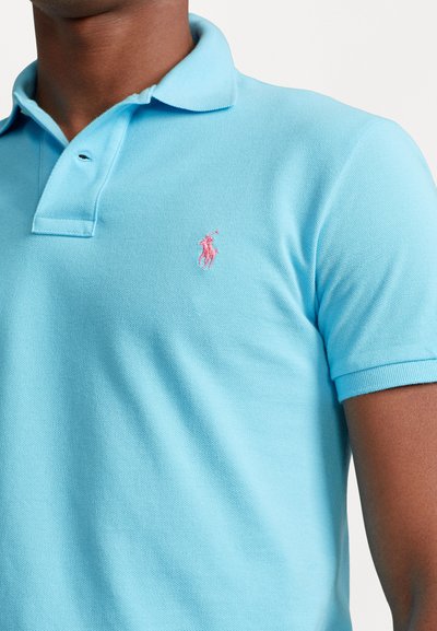 Heledsinine polo särk tekstuurilise mustriga, lühikeste varrukatega ja roosa tikandiga logo vasakul rinnaosas. Klassikaline kraediisain.
