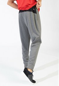 Grijze sportieve joggers met een zwarte tailleband, zachte textuur, tapered leg design en zijzakken. G gedragen met zwarte sneakers.