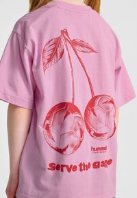 Rosa bomullströja med röda körsbärsgrafiker, ett par fotbollar och texten "Serve the game" under designen.