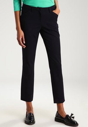 Pantalons noirs ajustés avec une coupe slim, dotés de poches avant et d'une texture lisse. Associés à un haut vert et à des mocassins noirs brillants.