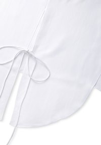 Witte stof met een gebogen zoom en twee lange linten die in een strik zijn geknoopt nabij de middennaad op een effen achtergrond.