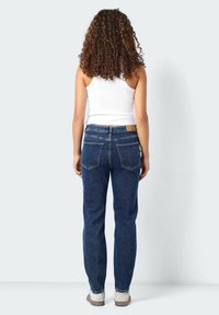 Tmavě modré džínové kalhoty rovného střihu, s pěti kapsami a světle hnědým koženým nášivkem na zadním pasu. Nosit s bílým topem.