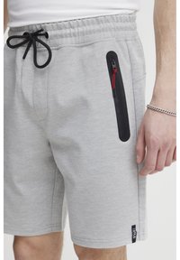 Shorts en molleton gris avec une taille élastique, cordon de serrage, poche zippée sur le côté avec des accents rouges, et une étiquette logo à l'ourlet. Tissu texturé.