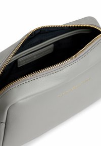 Borsa in pelle grigia con zip e dettagli dorati. L'interno è scuro e ha una superficie liscia. Logo impresso sulla parte anteriore.