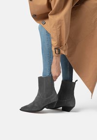 Gray suede ankle boots with pointy toes and elastic side panels. Features textured detailing and a low, block heel. Worn with blue jeans.