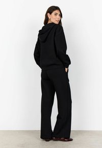 Felpa con cappuccio nera e pantaloni della tuta coordinati, realizzati in tessuto morbido, caratterizzati da una vestibilità ampia e tasche anteriori. Texture liscia con design casual.