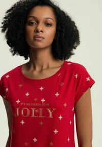 Czerwona koszulka z krótkim rękawem z złotym napisem "TO JEST PORA NA RADOŚĆ" oraz białymi wzorami płatków śniegu. Gładka tekstura materiału.