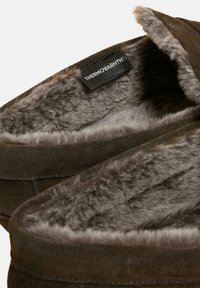 Brune ruskindssandaler med grå kunstpelsfor og et mærke, der siger "THERMOWARMTH." Blød tekstur med afrundet form og stikning.